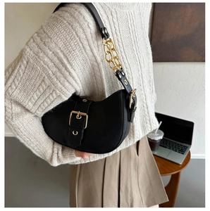 Detail of black crescent shoulder bag with large gold buckle and chain strap on model