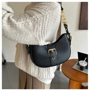 Detail of black leather half-moon shoulder bag featuring a gold chain and metal buckle