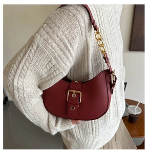Detail of dark red half-moon leather bag with gold buckle and chain shoulder strap
