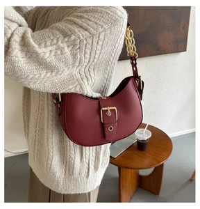 Close-up of a burgundy leather crescent bag with gold buckle and chain shoulder strap