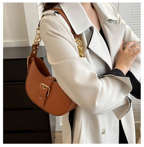 Detail of brown leather hobo bag with gold chain strap on a model in beige trench coat