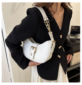 Detail of white half-moon shoulder bag with gold chain strap and belt buckle decor