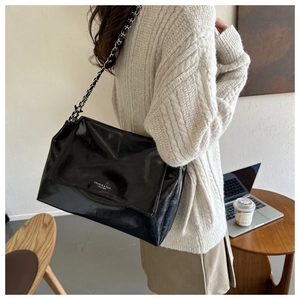 Detail of soft black patent leather shoulder bag with woven metal chain strap for women