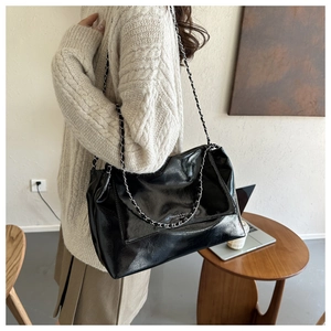 Detail of glossy black leather tote with silver metal chain strap and fashion logo print