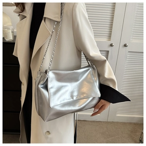 Detail of silver metallic leather tote bag with silver chain strap on white trench coat
