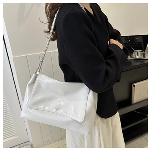 Close-up of white glossy leather tote bag with silver chain strap worn by a model