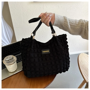 Detail of black pleated tote bag with golden fashion label and metal ring hardware