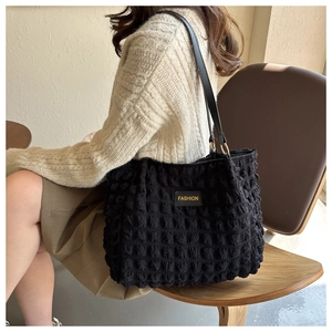 Detail of black pleated tote bag with bubble texture and yellow fashion logo label