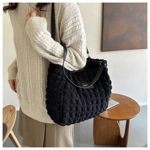 Detail of black textured tote bag with bubble fabric and fashion label on shoulder