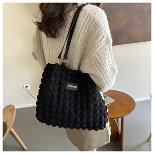 Detail of black pleated shoulder bag with embossed texture and FASHION label accent