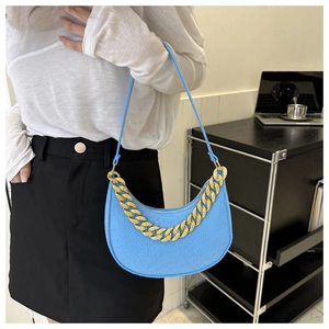 Detail of sky blue half-moon shoulder bag with gold chain strap worn by a model