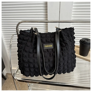 Detail of black pleated tote bag showing bubbled texture fabric and yellow FASHION patch