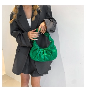 Detail of green hobo cloud bag with ruched pleats held by model in grey blazer