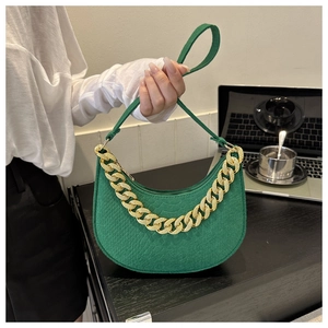 Detail of green hobo bag with crocodile texture and gold chain on an office desk
