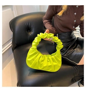 Neon green pleated handbag shown with a dark sweater and black leather skirt