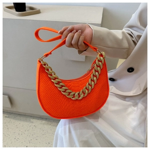 Detail of vibrant orange crescent bag with crocodile texture and gold chain strap
