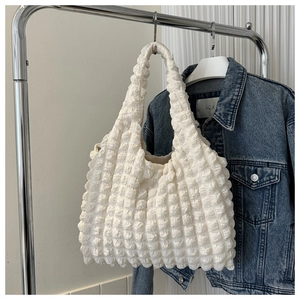 Détail du sac cabas blanc cassé à texture gaufrée suspendu sur un cintre métallique