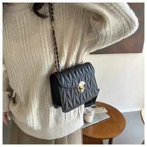 Detail einer schwarzen Stepptasche mit goldener Kette auf einem Holztisch-Arrangement
