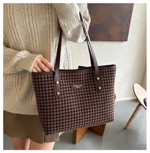 Close-up of houndstooth tote bag featuring leather straps and gold stud details