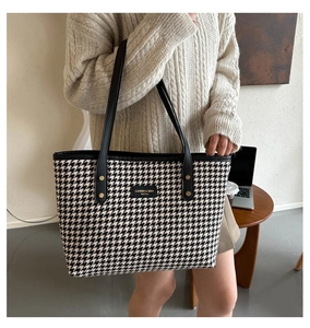 Detail of houndstooth tote bag with black leather trim and golden rivets on the front