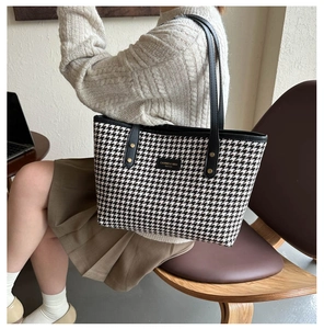 Detail of houndstooth tote bag featuring black leather trim and gold rivet accents