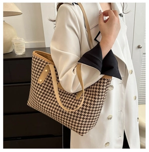 Detail of houndstooth tote bag with camel leather handles worn over a white trench coat