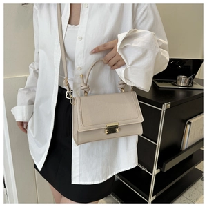 Detail of beige faux crocodile leather flap and gold rectangular lock on crossbody bag