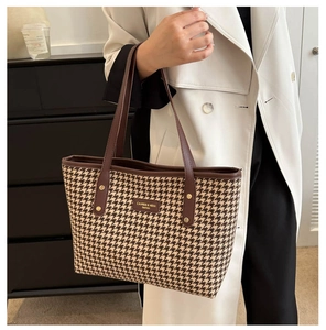 Detail of checkered tote bag with leather straps and golden logo plaque on woven fabric