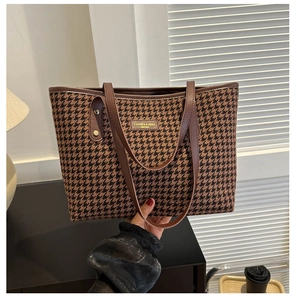 Detail of checkered tote bag with brown leather straps and embossed fashion brand logo