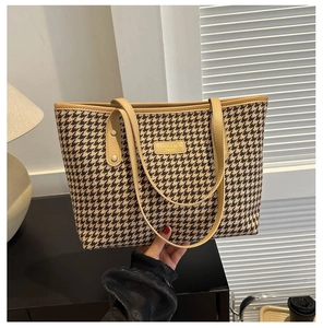 Close-up of houndstooth tote bag with khaki leather handles and brand logo patch