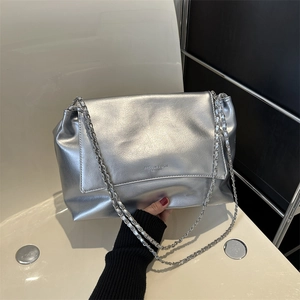 Silver metallic leather shoulder bag with chain strap and flap closure on a white chair