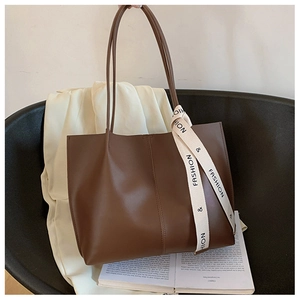 Detail of soft brown leather tote bag featuring decorative silk scarf on a handle