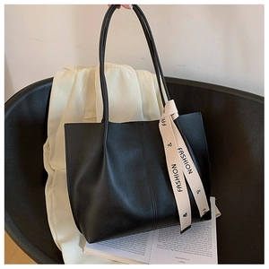 Close-up of black leather tote bag with a beige decorative ribbon on a black chair