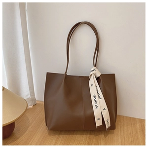 Detail of dark brown leather tote bag showing textured finish and decorative ribbon