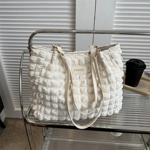 Chic off-white pleated tote bag with bubble texture and FASHION label on a glass shelf