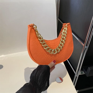 Orange croc-embossed crescent underarm bag with bold gold chain held in hand