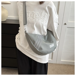Detail of grey crescent shoulder bag with white fashion tag and wide strap styling
