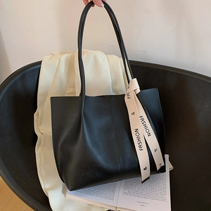 Minimalist black soft leather tote bag with elegant cream ribbon detail for daily commute