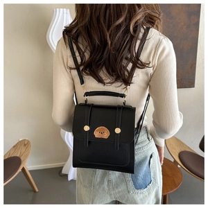 Detail of a black faux leather backpack featuring a cute brown plush puppy patch on the flap