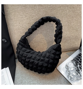 Dettaglio della borsa a spalla nera con trama a pieghe su sfondo lifestyle minimalista