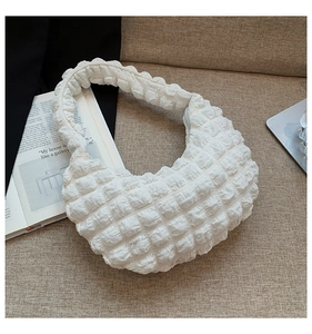 Dettaglio borsa hobo bianca con texture a bolle e tessuto a pieghe su fondo beige