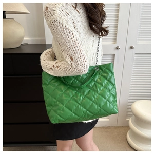 Close-up of a bright green quilted tote bag with chain strap worn by a model in a room
