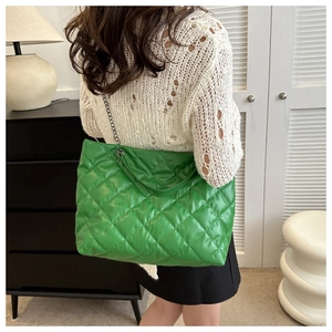 Detail of green quilted puffer shoulder bag with metal chain strap worn by a model