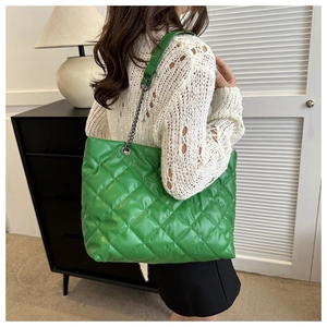 Green quilted tote bag with chain strap shown on shoulder for size and style detail