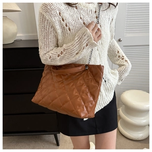 Brown quilted tote bag detail with metal chain strap on model in stylish outfit