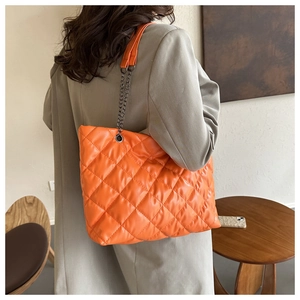 Orange quilted tote bag with black chain strap worn by a model in a casual indoor setting