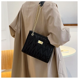 Detail of black quilted leather shoulder bag with gold chain strap on trench coat