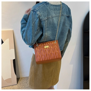 Close-up of brown quilted chain shoulder bag with gold metal lock on female model
