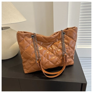 Detail of a brown quilted tote bag with silver chain straps on a black surface