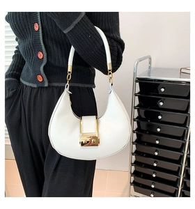 Close-up of white crescent handbag featuring gold metal buckle and sleek leather finish